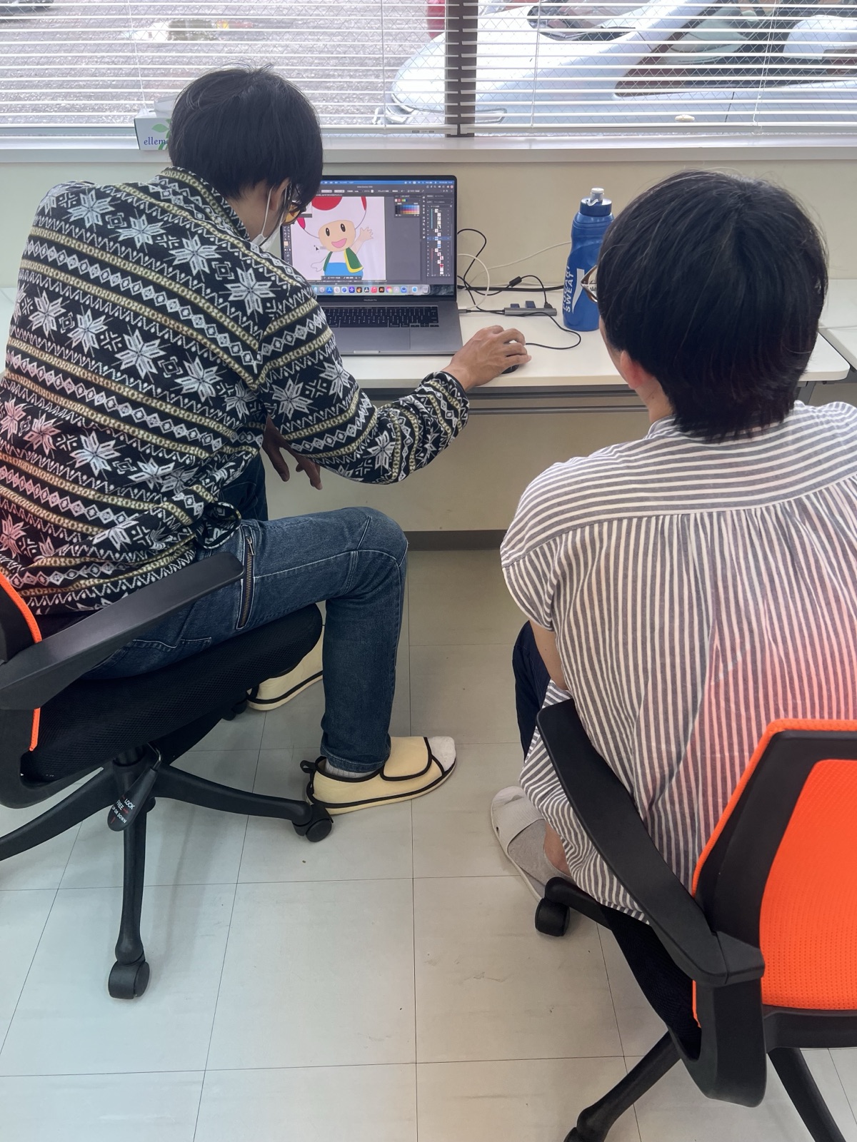 就労継続支援B型ALIIで、パソコンを使ってキャラクターのイラストを制作する利用者さんと、隣で見守るスタッフ