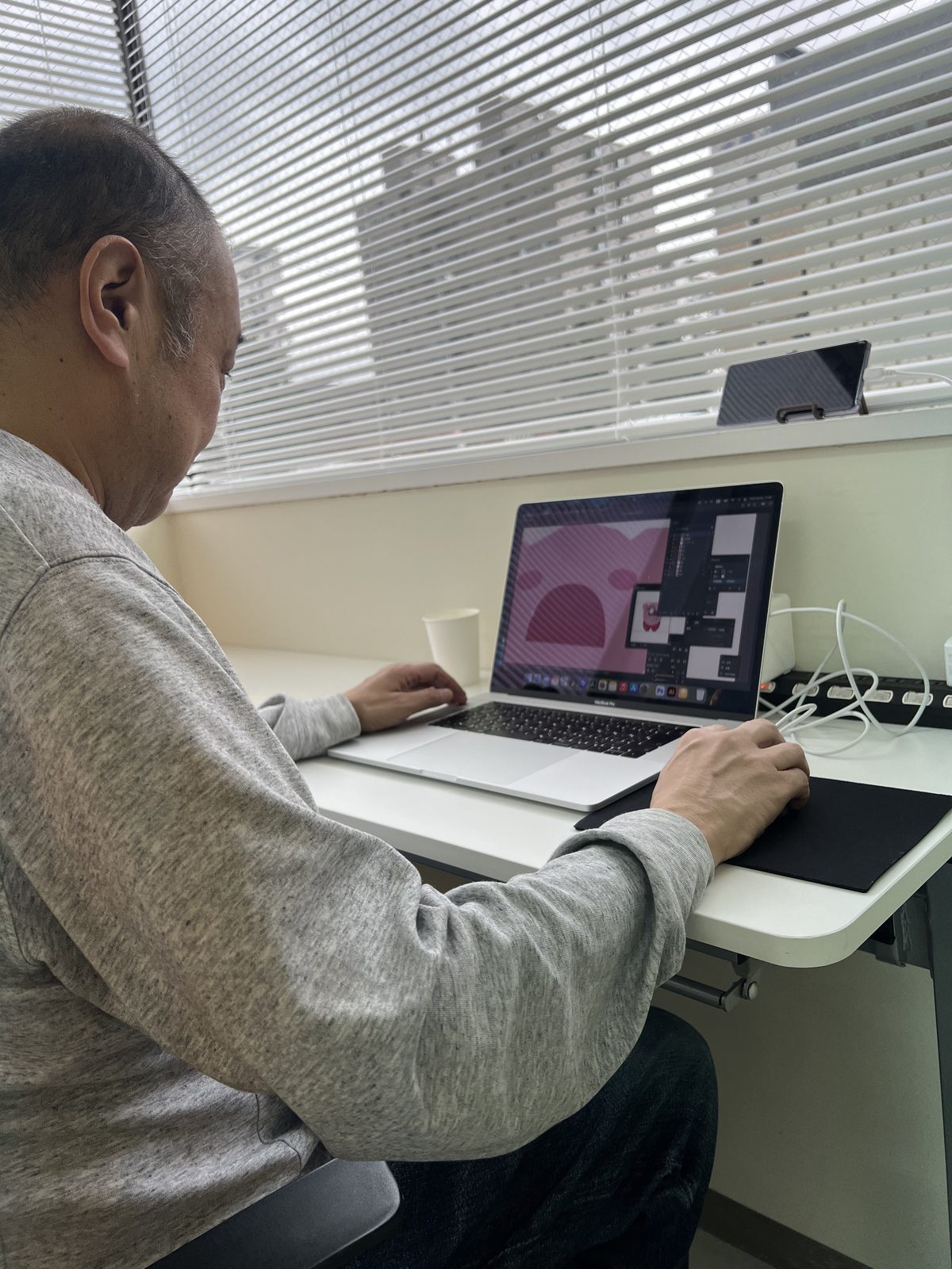 窓際でノートパソコンを使ってイラスト制作に集中する利用者さん